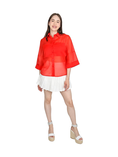 Mujer vistiendo blusa de organza roja con manga kimono y cuello, combinada con falda blanca plisada.