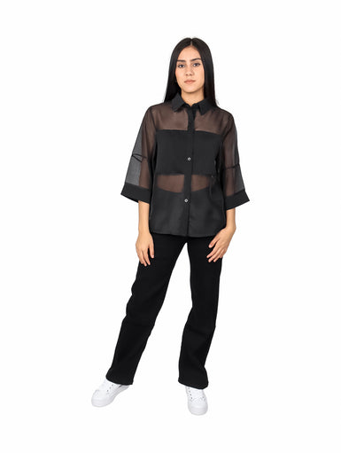 Mujer vistiendo blusa de organza negra con mangas estilo kimono y detalles transparentes.