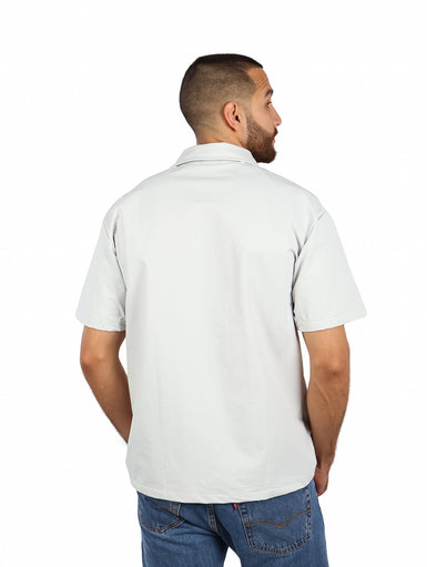 Hombre vistiendo camisa de manga corta color gris claro con bolsillo superior con cierre zipper.