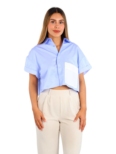 Mujer vistiendo camisa azul de rayas con un bolsillo blanco frontal y pantalones beige.