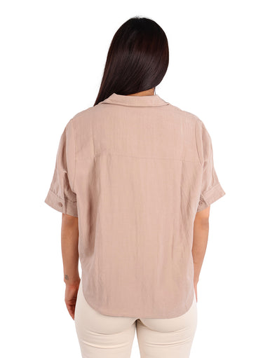 Mujer vistiendo una camisa de manga corta color khaki con botones frontales y pantalones claros.