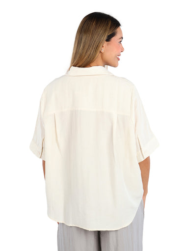 Mujer vistiendo una camisa de color linen con manga corta y botones frontales, estilo casual.
