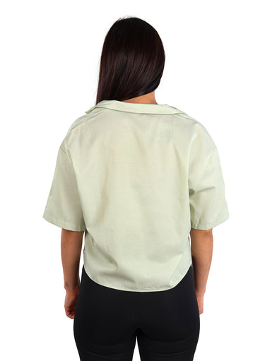 Mujer vistiendo una camisa de manga corta color verde claro con botones y cuello abierto.