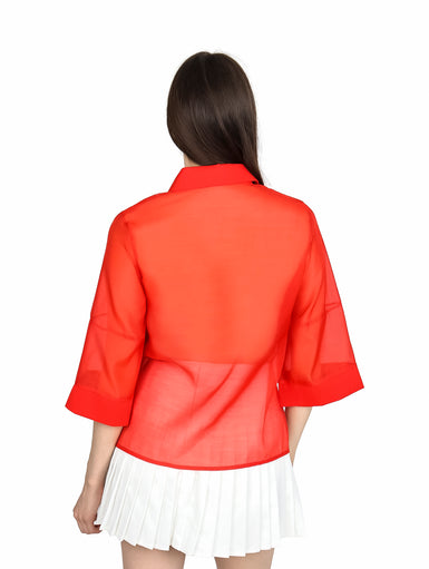 Mujer vistiendo blusa de organza roja con manga kimono y cuello, combinada con falda blanca plisada.