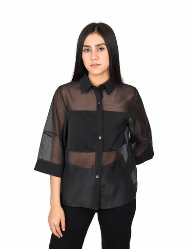 Mujer vistiendo blusa de organza negra con mangas estilo kimono y detalles transparentes.