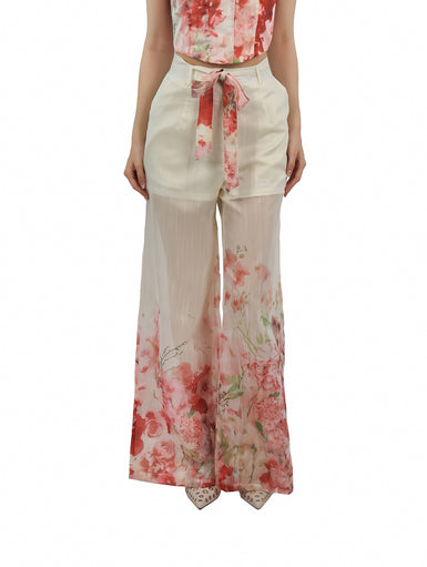 Pantalón ancho color beige con estampado floral en tonos rojos y rosas, incluye lazo en la cintura.