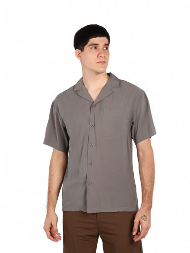 Hombre vistiendo una camisa básica de color gris con manga corta, cuello abierto y un bolsillo en el pecho.