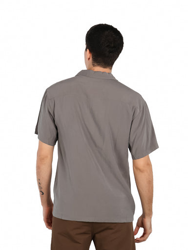 Hombre vistiendo una camisa básica de color gris con manga corta, cuello abierto y un bolsillo en el pecho.