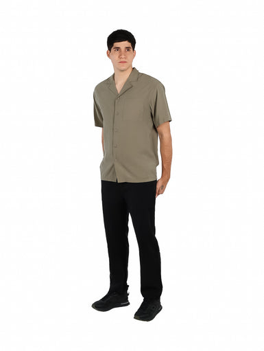Hombre vistiendo una camisa básica de manga corta en color verde militar con cuello abierto y un bolsillo frontal.