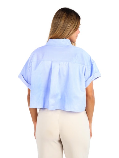 Mujer vistiendo camisa azul de rayas con un bolsillo blanco frontal y pantalones beige.
