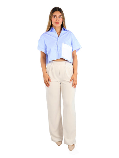 Mujer vistiendo camisa azul de rayas con un bolsillo blanco frontal y pantalones beige.