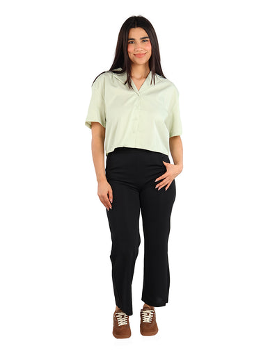 Mujer vistiendo una camisa de manga corta color verde claro con botones y cuello abierto.